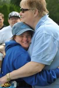 woman in aim services hat hugs woman in blue polo