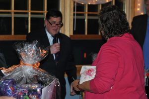 man speaking in microphone with woman in pink listening next to raffle basket
