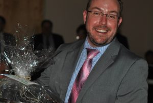 man in gray suit smiling with gift basket