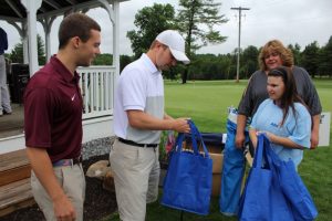 man in white polo hands out blue aim services tote bags