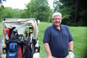 man in blue smiles for camera next to golf cart
