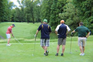 three golfers watch another tee off