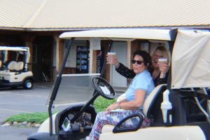two women toasting beers in golf cart