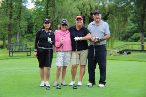 group of three women and a man smiling with clubs on tee box