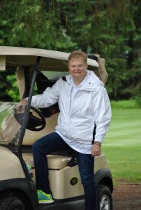 woman in white jacket poses with one foot in golf cart