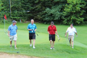 four golfers leaving the green with clubs in hand