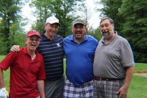 group of four golfers laughing hard and smiling for photo