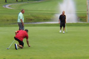 three men on a green, one bending down to mark his ball