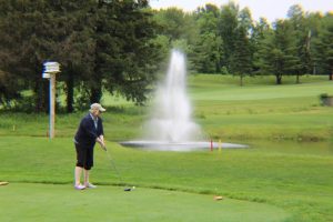 woman stands, ready to tee off with large fountain in background