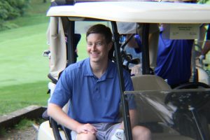 man in golf cart smiles while sitting shotgun