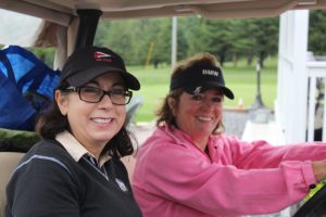 two women in black hats smiling while sitting in golf cart