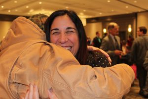 woman with large smile hugging man in brown jacket