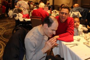 man in red sweater offering a hand to another man at table