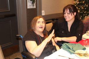 woman in wheelchair with multiple necklaces smiling as another woman looks on