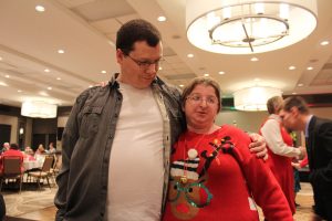 man and woman with arms around one another, man seems to be questioning womans christmas sweater