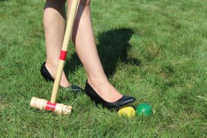 close shot of woman putting black heel on croquet balls