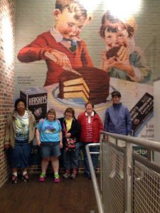 group of five women pose next to hershey mural