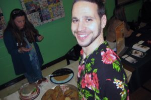 man in floral pattern shirt takes a selfie at dessert table