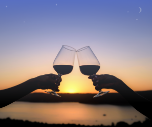 Silhouette of two wine glasses cheersing over a sunset on a lake