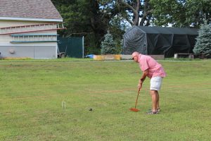 man in red checkered shirt hitting croquet ball towards wicket