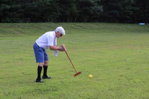 man with long socks, shorts and tie following through on croquet shot