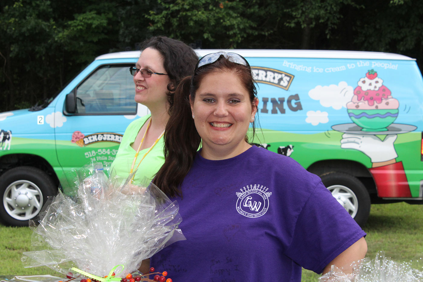 woman in purple tshirt smiles with raffle baskets