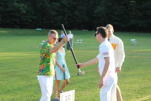 commissioner of croquet hands special mallet to man in parrot shirt