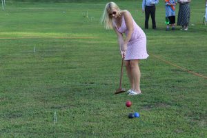 woman in pink dress tries hitting croquet ball over two other balls