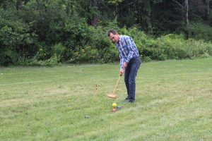 man in flannel hitting and splitting croquet balls