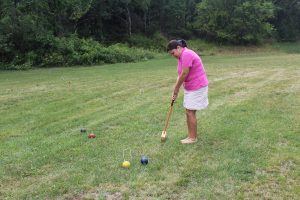 woman in hot pink polo smacking croquet ball towards wicket