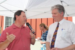 man in red polo speaking to another man using microphone