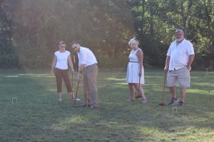 four people wearing white tops beginning their croquet game
