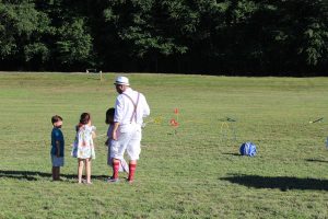 man with suspenders and high socks talking to children on croquet field