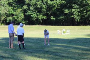 three people watching woman with perfect form hit croquet ball