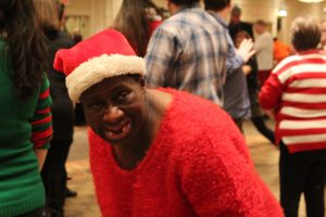 woman smiles on dance floor while wearing santa hat and fuzzy red sweater