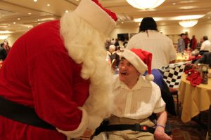 santa greeting party goer in wheelchair with santa hat smiling