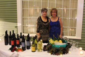 two women standing behind table with multiple wine bottles, some being chilled