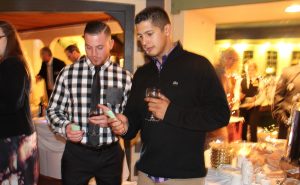 two men drinking wine and looking at green cards in hand