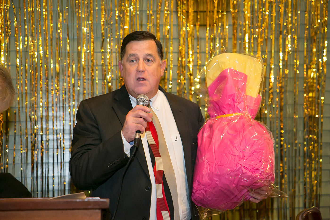 man in suit speaking on microphone with pink basket