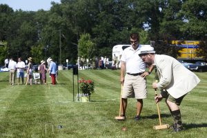 man carefully lines up croquet mallet to punch one through the wickets
