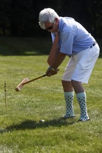 man dressed in goofy high socks rearing back to smack croquet ball
