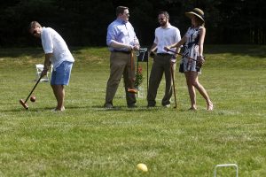 group of four croquet players chat while one strikes ball at 4th annual croquet on the green