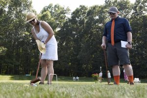 woman goes for the wicket while man in orange high socks watches on