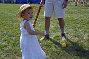 baby girl in white dress and hat holds croquet stick