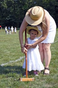 mom teaching little girl the correct way to hold a croquet stick, which is bigger than her