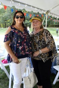 woman in yellow visor smiles with woman in sunglasses under tent at 4th annual croquet on the green