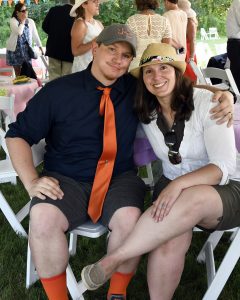 man with orange tie smiles with woman wearing hat