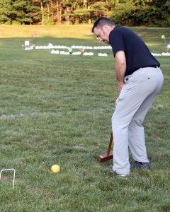 man in black swings at yellow croquet ball