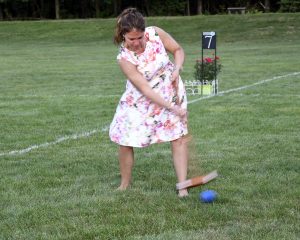 woman swiping at blue croquet ball on yard