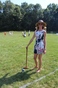 woman in stylish dress and hat poses with her mallet and blue ball